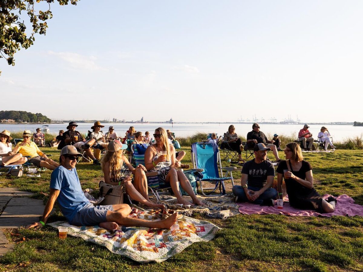 A group of people sitting in chairs and on blankets in front of the water enjoying the  sunset